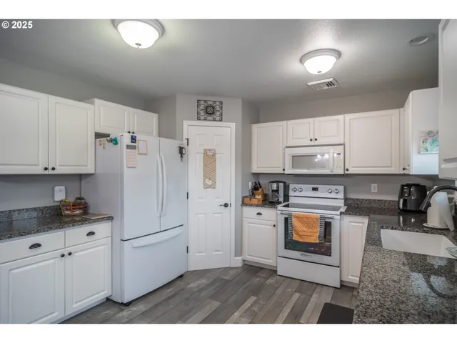 a kitchen with stainless steel appliances granite countertop a refrigerator sink stove and white cabinets