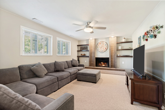 9832 Falconhurst Drive Sandy, UT 84092 - Photo 19 of 29 Living area featuring a brick-surround fireplace with hearth, built-in shelving, twin windows, and a ceiling fan with integrated lighting