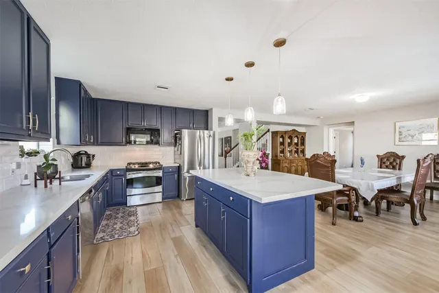 a large kitchen with stainless steel appliances granite countertop a stove oven a sink dishwasher and a refrigerator with wooden floor