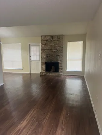 an empty room with wooden floor fireplace and windows