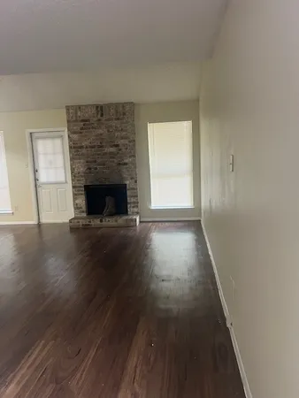 an empty room with wooden floor fireplace and windows