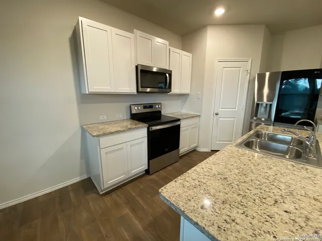 a kitchen with granite countertop a sink a stove top oven a counter space and cabinets