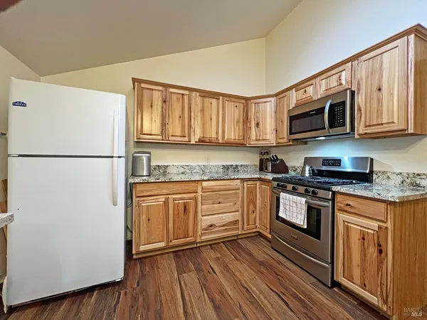 a kitchen with stainless steel appliances granite countertop a refrigerator a stove top oven a sink and dishwasher with wooden floor