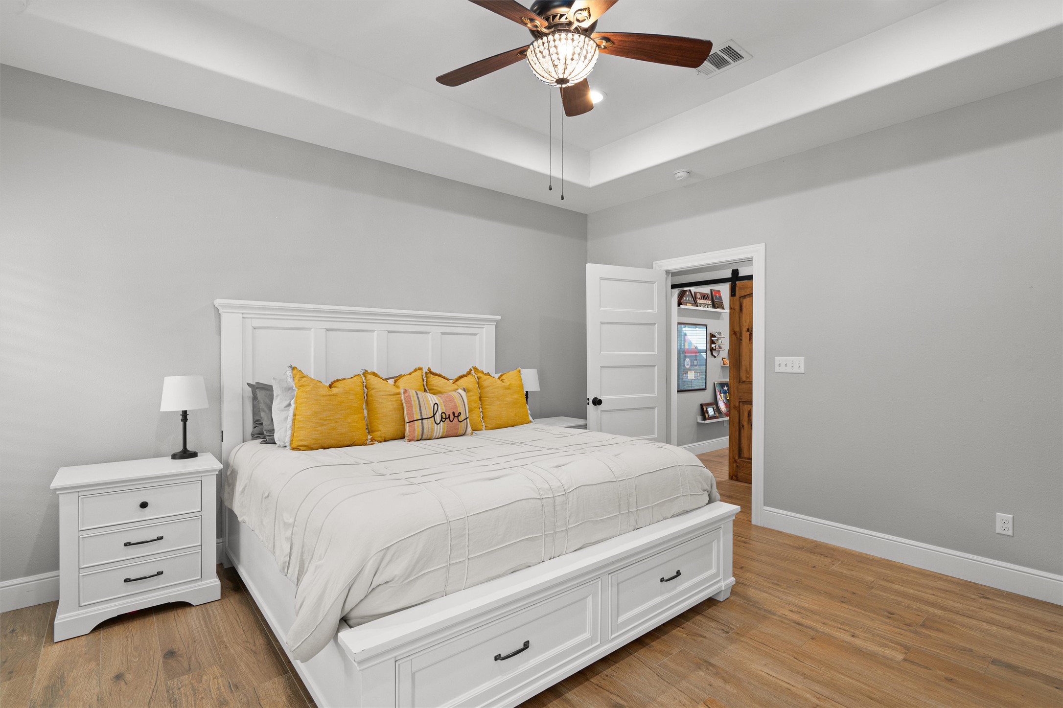 136 Fawn Hollow Elgin, TX 78621 - Photo 15 of 40 Primary bedroom featuring wood-finish flooring, a tray ceiling, and a ceiling fan with integrated lighting