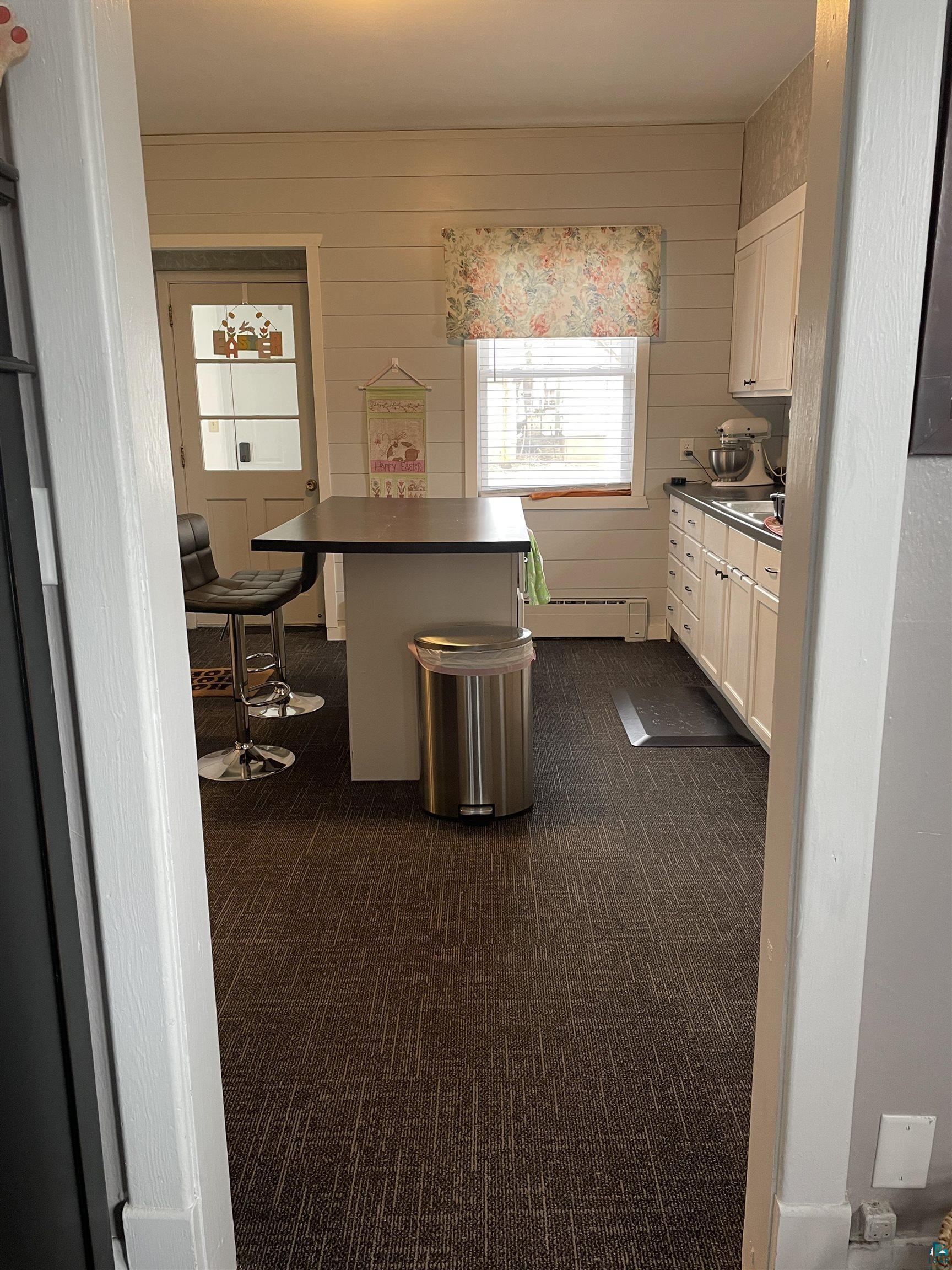203 3rd Street South Virginia, MN 55792 - Photo 4 of 22 Kitchen featuring dark countertops, dark carpet, a breakfast bar, white cabinetry, and wooden walls