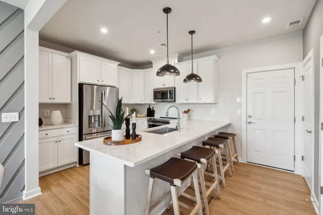 a kitchen with stainless steel appliances a stove a sink a refrigerator a center island and a wooden floor