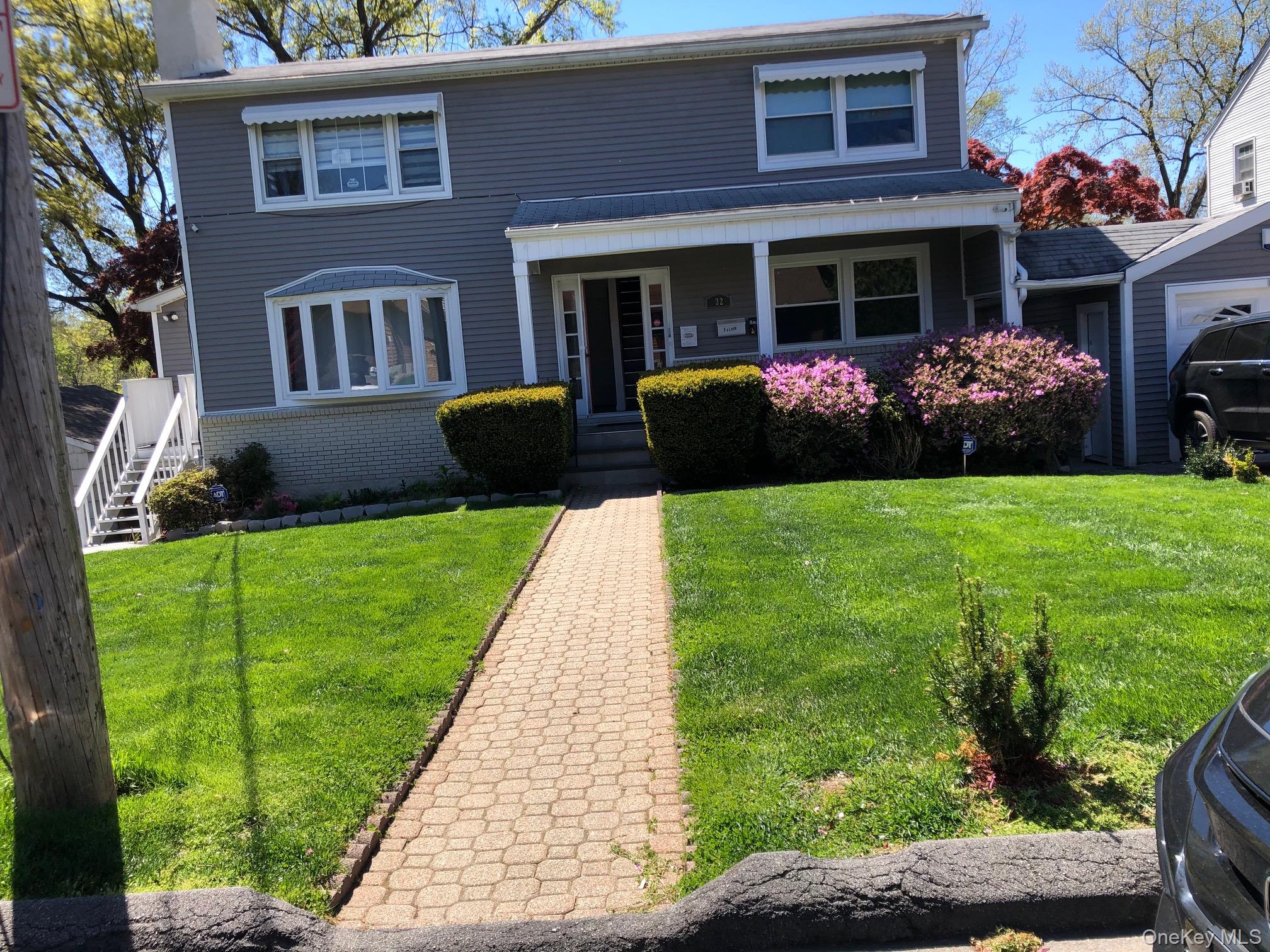 View of front facade with brick siding, a porch, a chimney, and a front yard