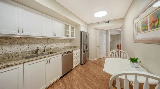 a kitchen with stainless steel appliances granite countertop a sink dishwasher a stove a refrigerator with white cabinets and wooden floor