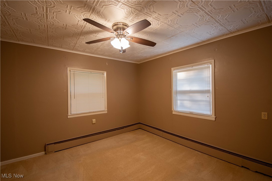 9719 Angling Road Wakeman, OH 44889 - Photo 19 of 39 Empty room featuring an ornate ceiling, ornamental molding, baseboard heating, light colored carpet, and ceiling fan