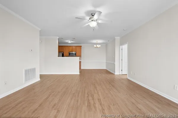 a view of an empty room with wooden floor and a ceiling fan