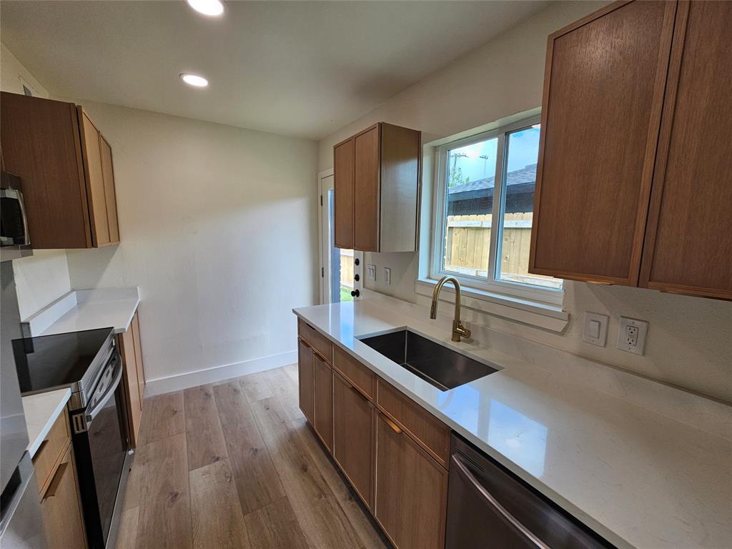 1725 R Avenue, Unit 1727 Plano, TX 75074 - Photo 5 of 20 Bright kitchen featuring light wood-finish cabinetry, white countertops, stainless steel appliances, a deep basin sink with a gold-finish faucet, and wood-finish flooring