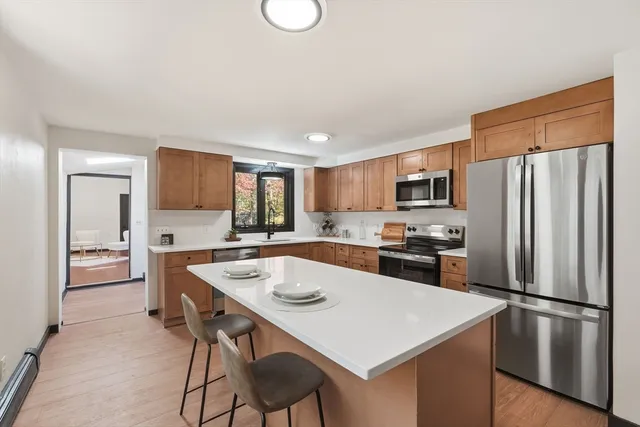 a kitchen with stainless steel appliances a stove a sink a refrigerator white cabinets and wooden floor