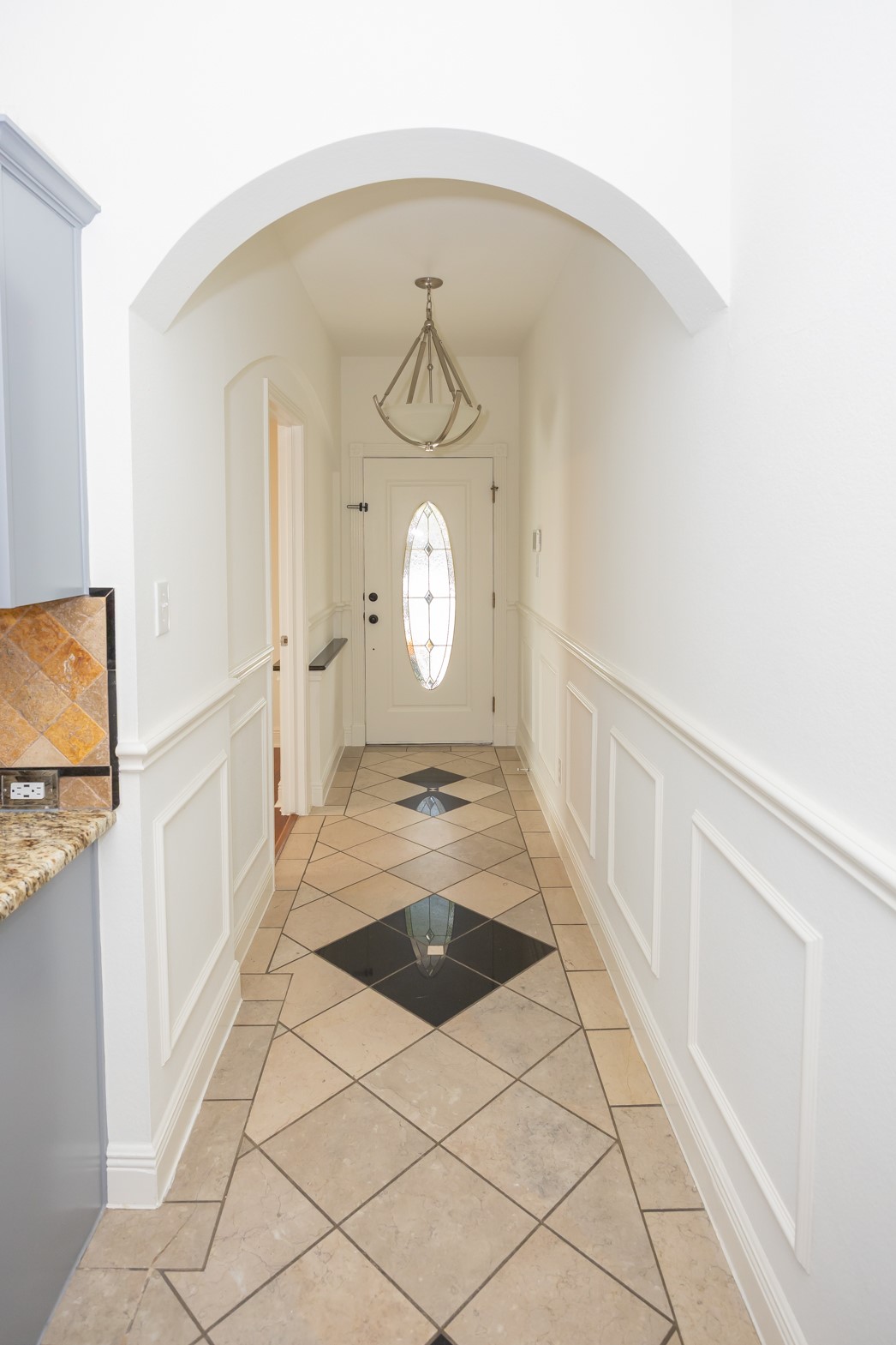 11500 Dimmit Street Manor, TX 78653 - Photo 2 of 14 Arched entryway featuring wainscoting, a decorative light fixture, and a tile floor with a diamond pattern