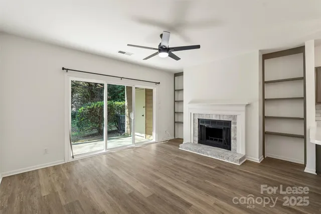 a view of an empty room with wooden floor fireplace and a window