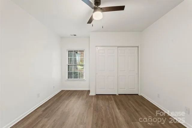 an empty room with wooden floor ceiling fan and windows