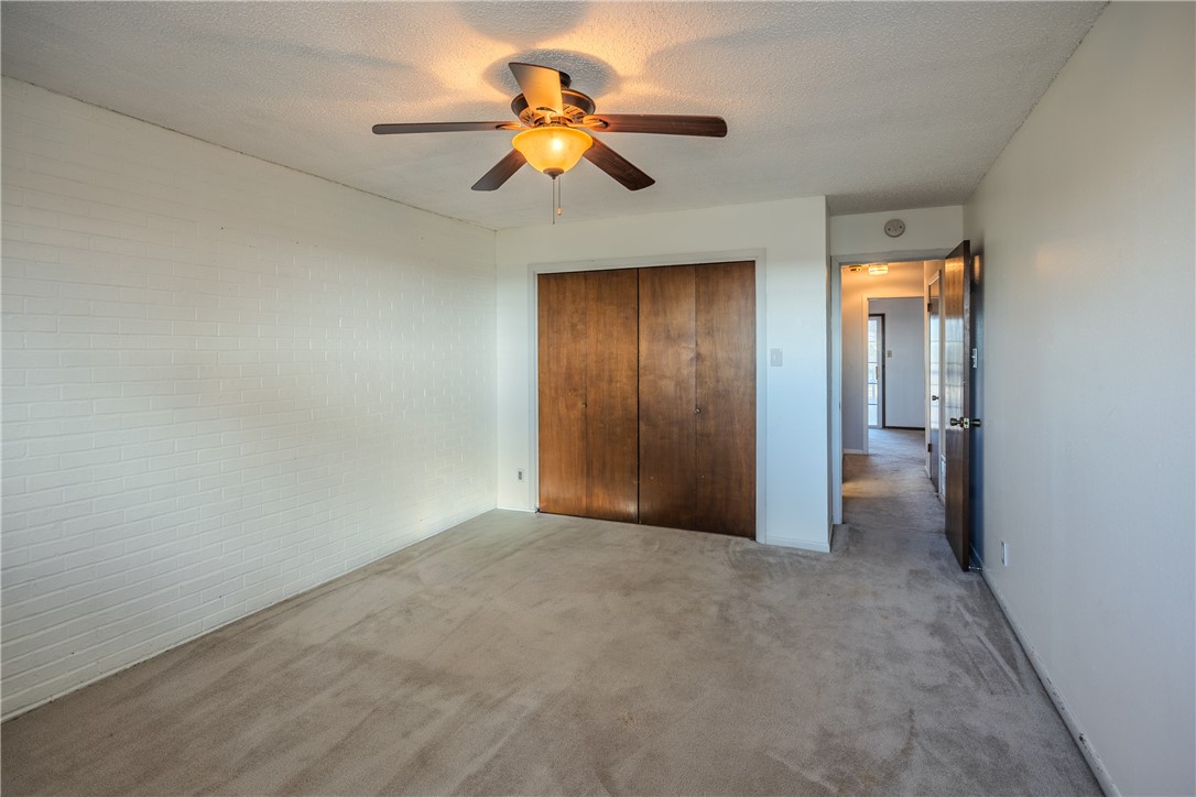 2002 South Lubbock Street Brenham, TX 77833 - Photo 22 of 26 Unfurnished bedroom with carpet flooring, a textured ceiling, ceiling fan, brick wall, and a closet