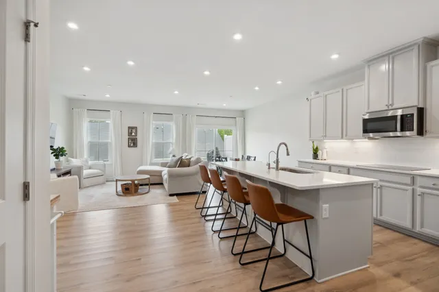 a living room with stainless steel appliances kitchen island granite countertop a sink a table and chairs with wooden floor