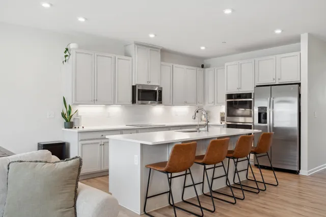 a kitchen with stainless steel appliances granite countertop a stove a sink a microwave a refrigerator and white cabinets with wooden floor