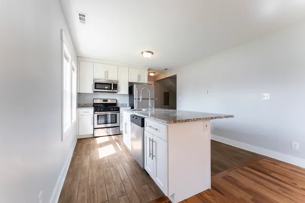a kitchen with stainless steel appliances a microwave a stove a sink dishwasher a refrigerator and white cabinets with wooden floor