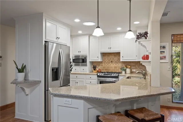 a kitchen with kitchen island a refrigerator a stove a sink and white cabinets with wooden floor