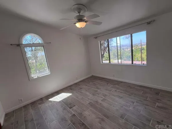 an empty room with wooden floor chandelier fan and windows
