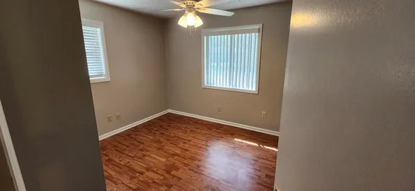 an empty room with wooden floor fan and windows