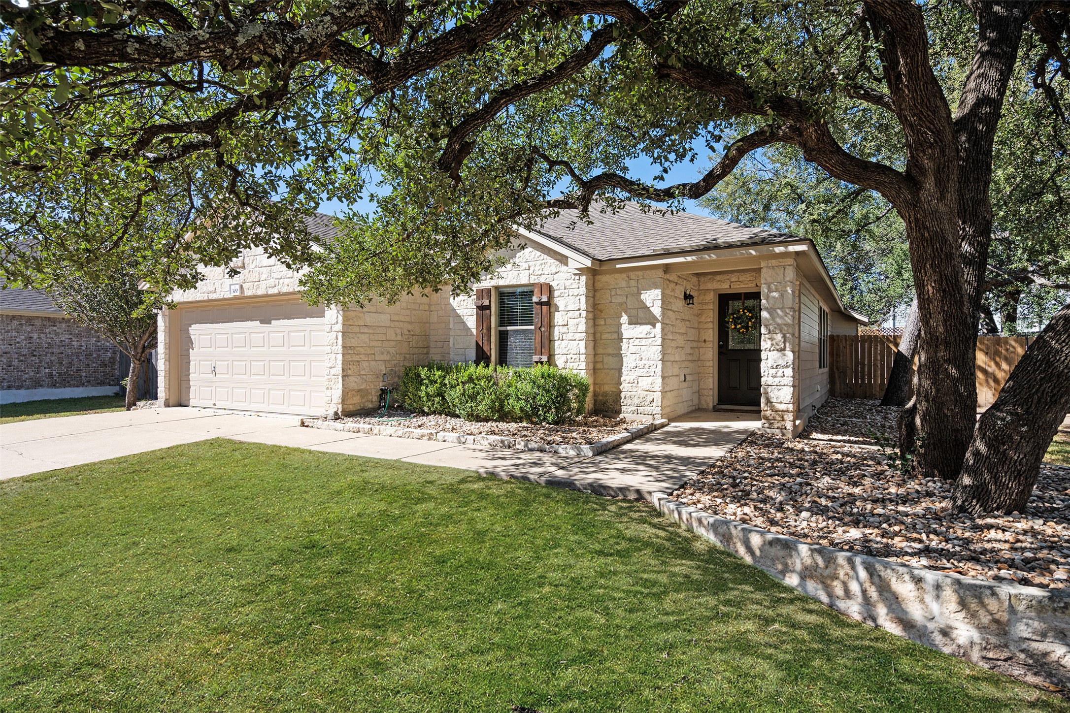 View of front of home featuring driveway, stone siding, an attached garage, and roof with shingles
