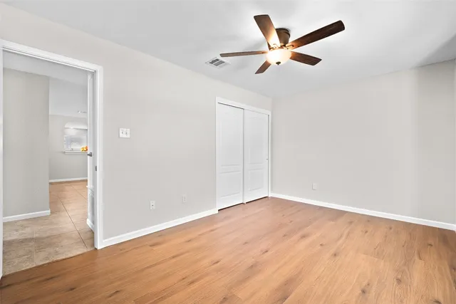 an empty room with wooden floor ceiling fan and window