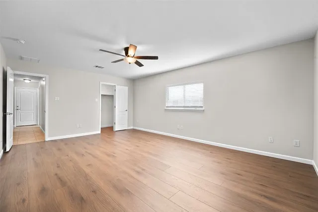 an empty room with wooden floor chandelier fan and windows