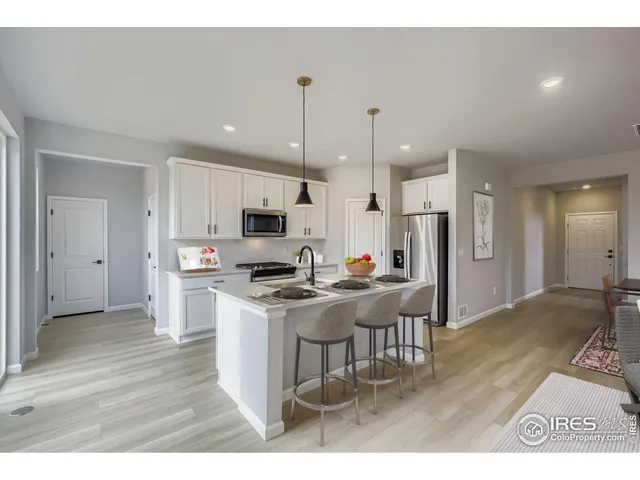 a kitchen with stainless steel appliances kitchen island granite countertop a refrigerator a stove a sink a microwave oven with white cabinets and wooden floor