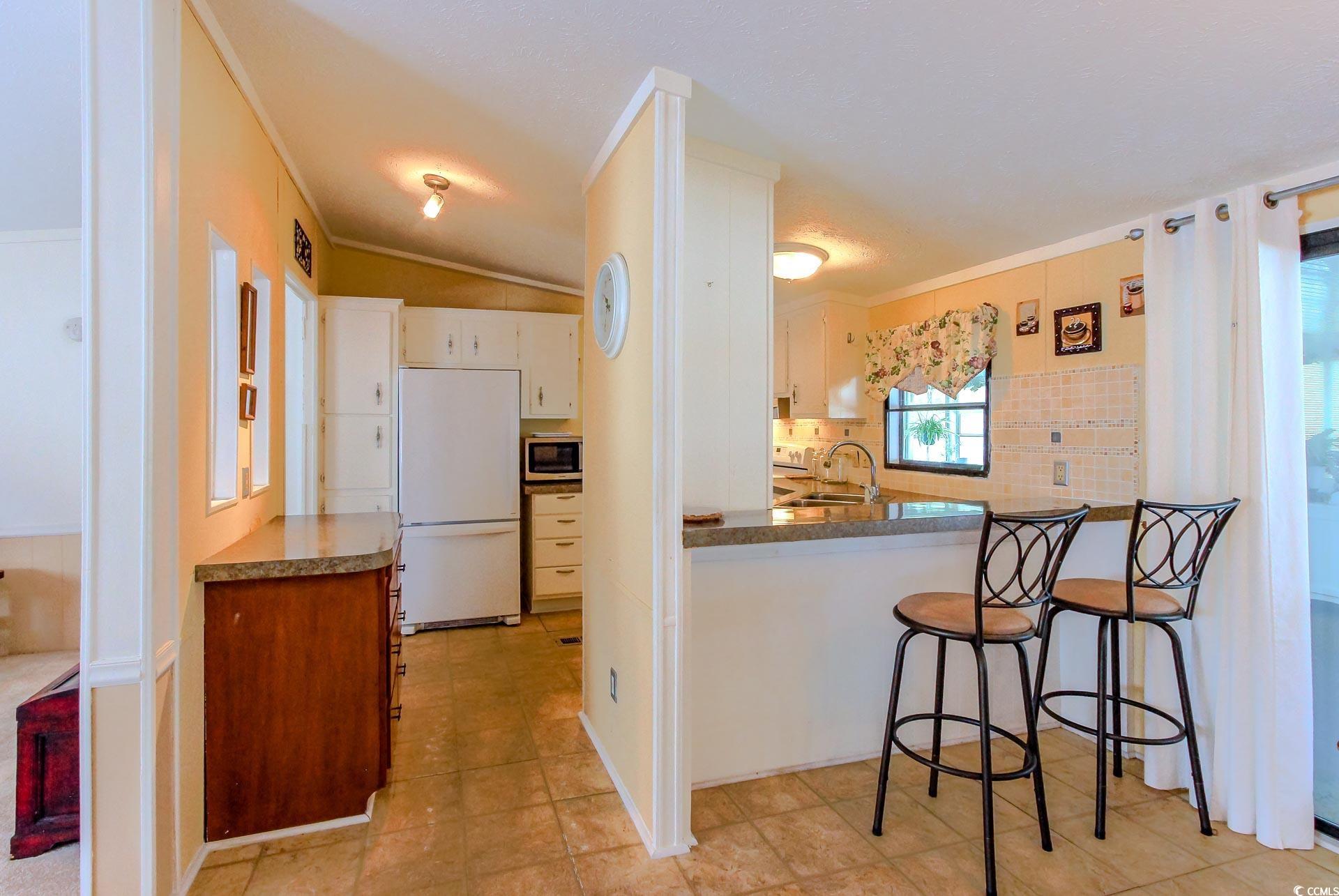 163 Crooked Island Circle Murrells Inlet, SC 29576 - Photo 11 of 40 Kitchen with freestanding refrigerator, a kitchen breakfast bar, tasteful backsplash, crown molding, and stainless steel microwave