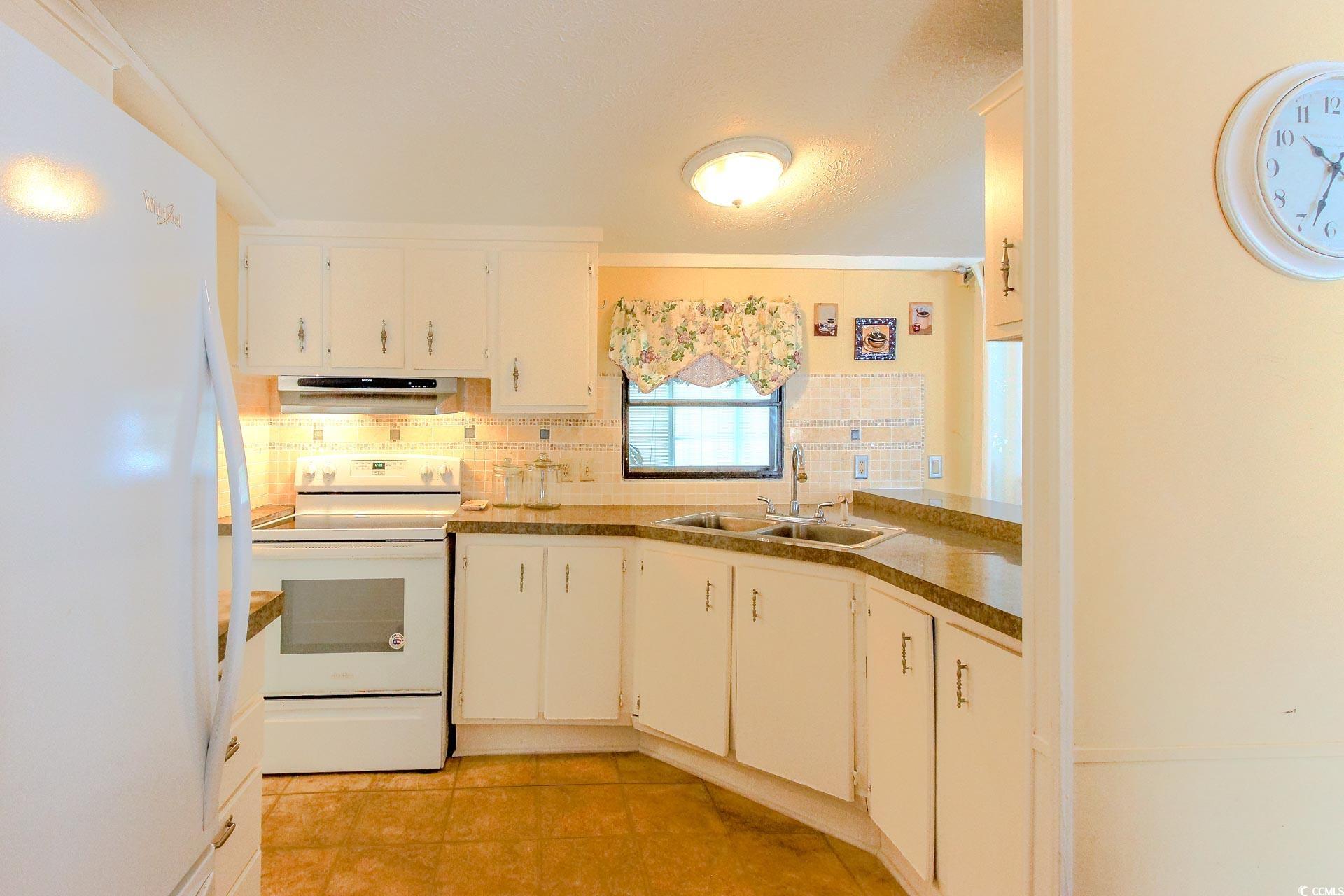 163 Crooked Island Circle Murrells Inlet, SC 29576 - Photo 12 of 40 Kitchen featuring white appliances, backsplash, white cabinets, under cabinet range hood, and light tile patterned flooring