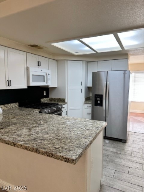 2152 Falcon Pointe Lane Henderson, NV 89074 - Photo 8 of 11 Kitchen featuring stainless steel appliances, dark stone counters, a peninsula, white cabinets, and wood finish floors