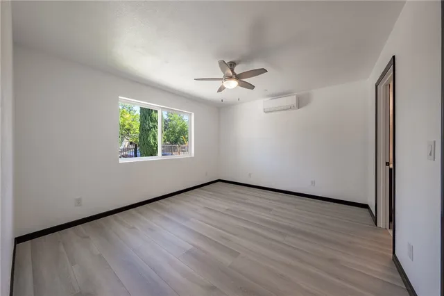 an empty room with wooden floor chandelier fan and windows