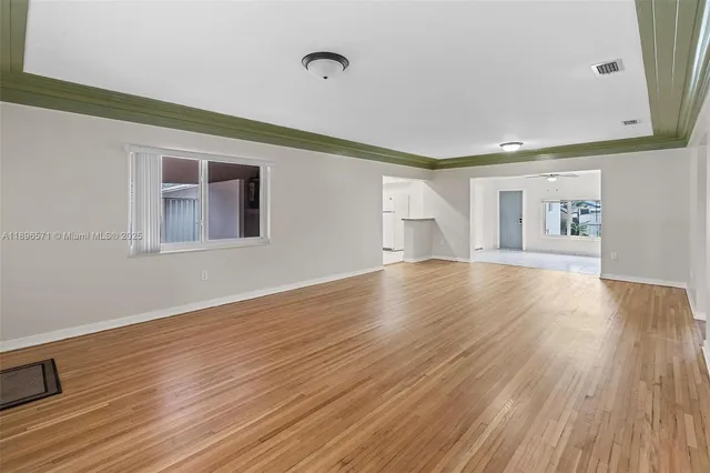 a view of a kitchen and an empty room with wooden floor and a window