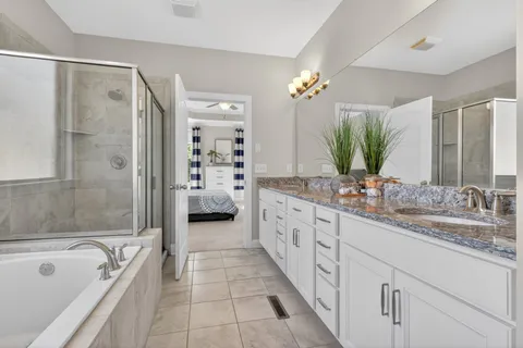 a spacious en suite bathroom with a granite countertop double vanity sink a large mirror a bathtub and shower