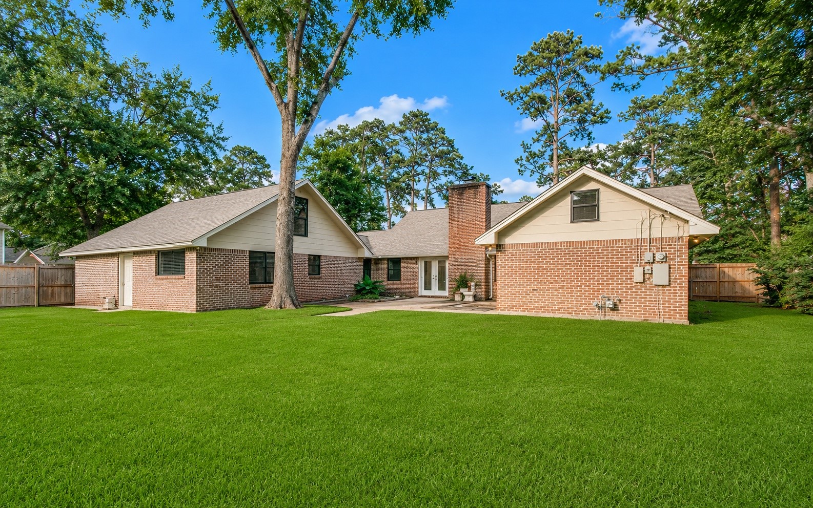 1801 Benbow Way Houston, TX 77080 - Photo 31 of 32 This photo showcases a charming brick home with a spacious, well-maintained backyard. The house features a large gable roof, a chimney, and a patio area. The yard is fenced, offering privacy and surrounded by mature trees, perfect for outdoor activities.