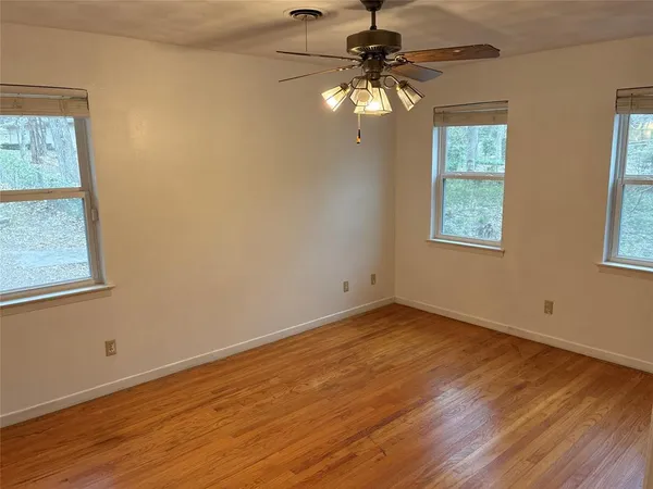 an empty room with wooden floor fan and windows