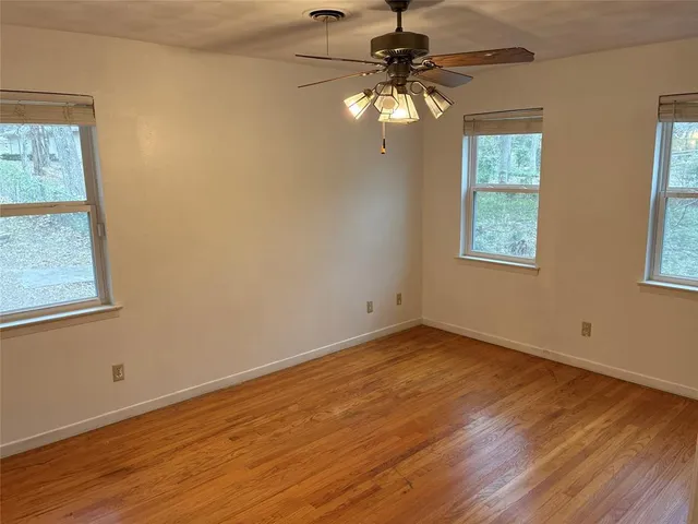 an empty room with wooden floor fan and windows