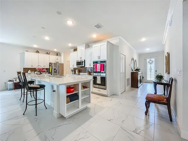 a living room with stainless steel appliances kitchen island granite countertop a table chairs and a refrigerator