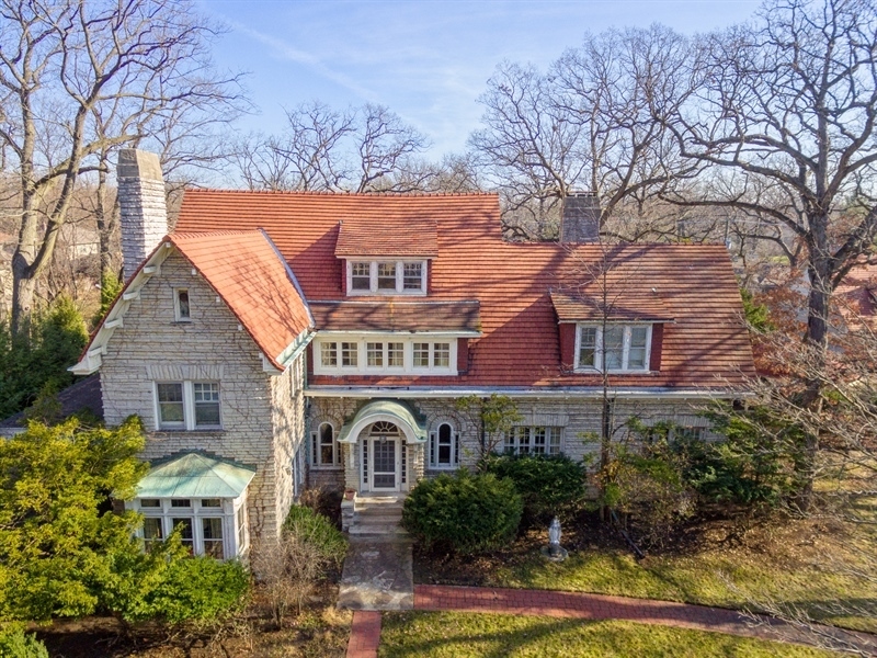 a view of a brick house with large windows and a yard with plants and large trees