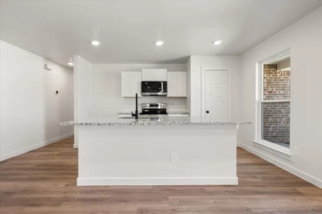 a view of kitchen with stainless steel appliances granite countertop a stove a sink a refrigerator and white cabinets with wooden floor