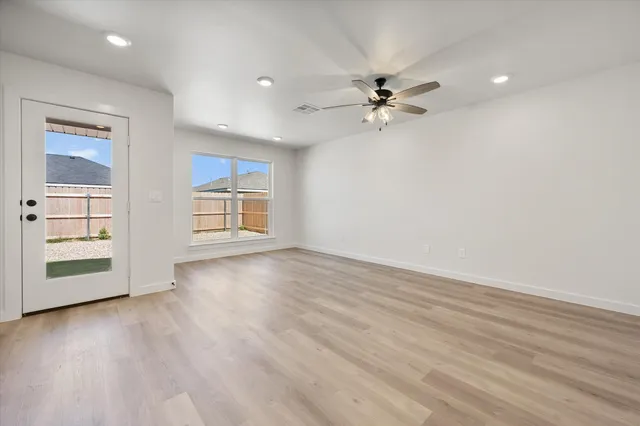 an empty room with wooden floor chandelier fan and windows