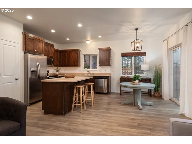 a kitchen with stainless steel appliances kitchen island granite countertop a refrigerator a stove a sink a dining table and chairs with wooden floor