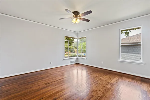an empty room with wooden floor chandelier fan and windows