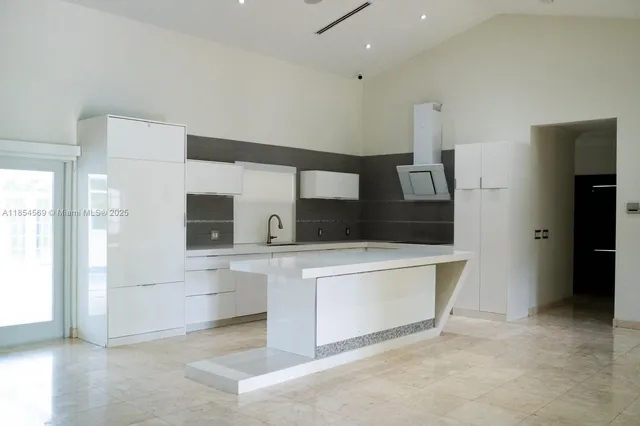 a large white room with stainless steel appliances kitchen island granite countertop a refrigerator and a sink