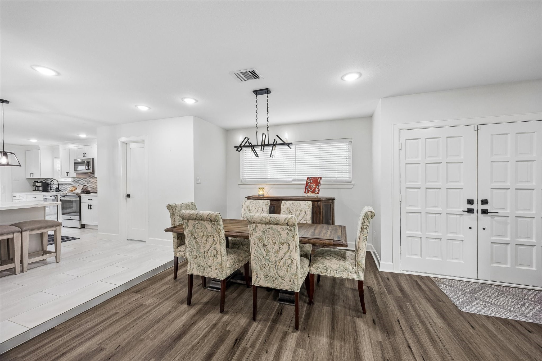 1420 Indiana Street Houston, TX 77006 - Photo 5 of 31 This photo showcases a bright, open dining area. The space features modern lighting and wood flooring, connecting seamlessly to a white kitchen with an island and barstools. The entrance has a double-door design, enhancing the home's welcoming appeal.