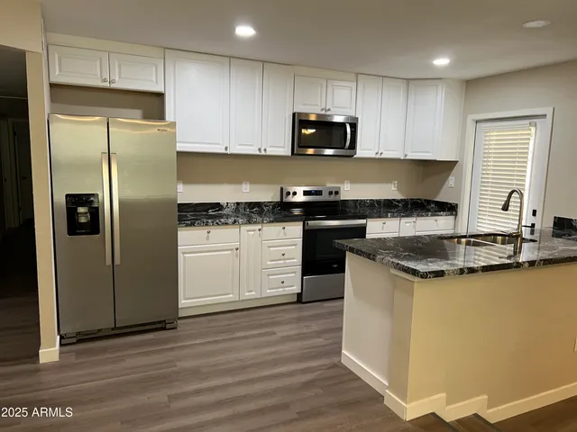 a kitchen with stainless steel appliances granite countertop white cabinets a refrigerator a sink a stove a microwave and wooden floors