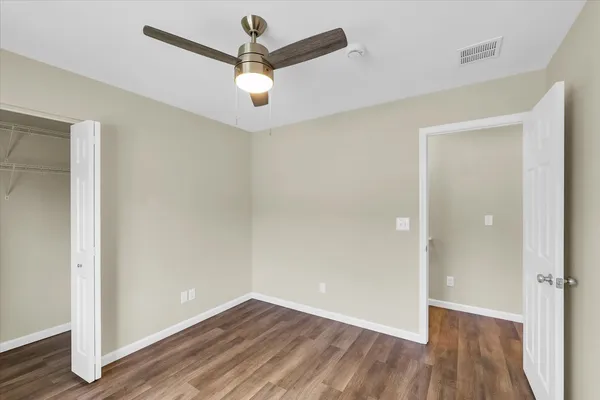 an empty room with wooden floor ceiling fan and windows