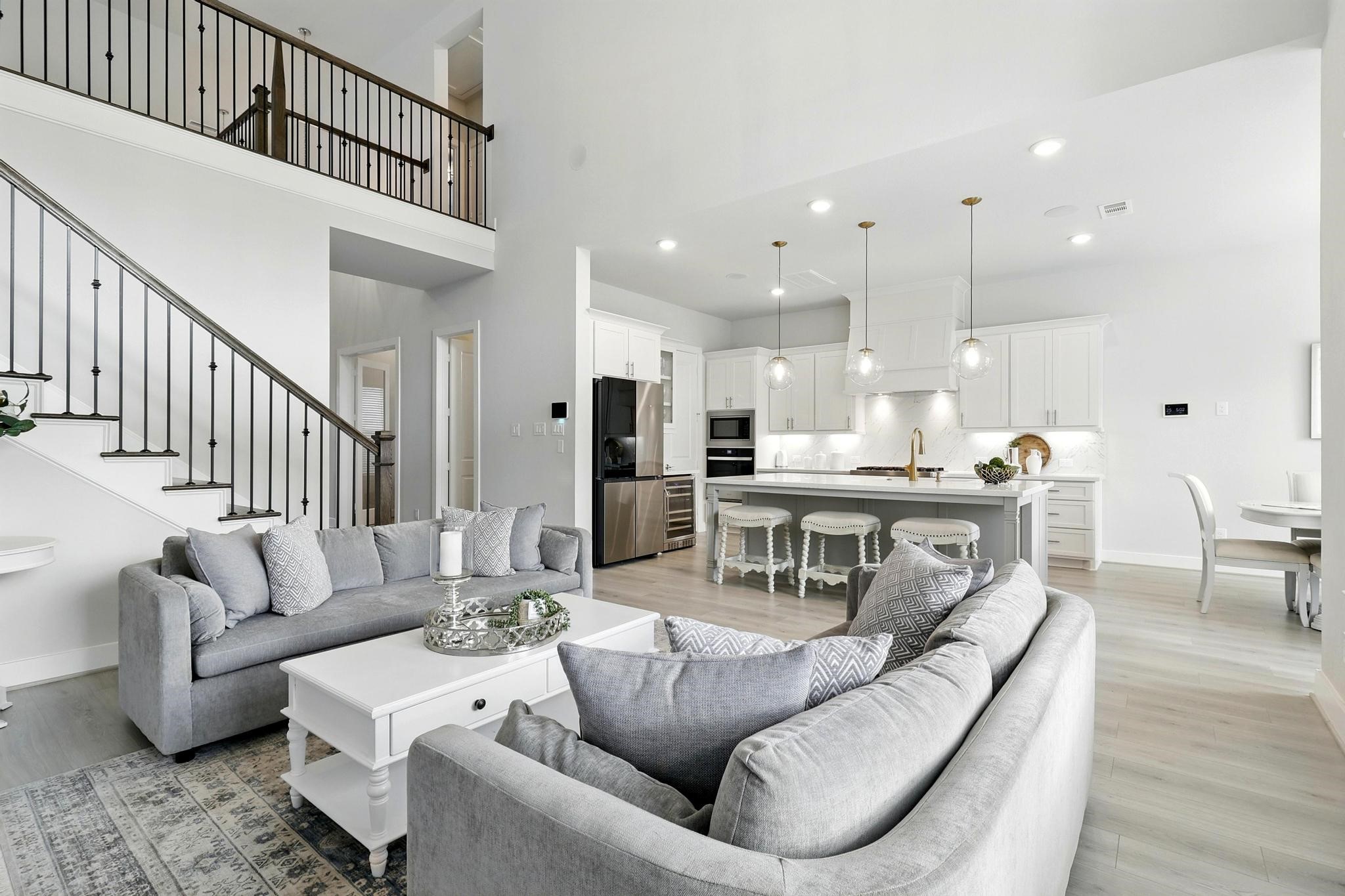 26923 Arethusa Court Spring, TX 77389 - Photo 6 of 44 This open-concept living area features a modern kitchen with a large island, elegant pendant lighting, and stainless steel appliances. The space is bright and airy, with high ceilings, A staircase with a wrought iron railing leads to an upper level, enhancing the home's spacious feel.